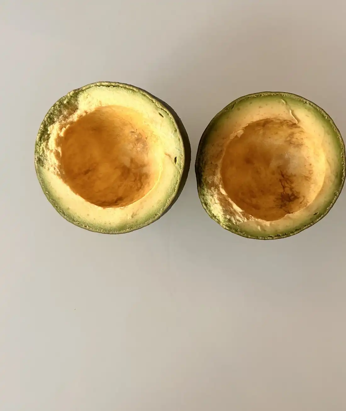 Two avocado halves with the flesh scooped out, on a pale grey surface