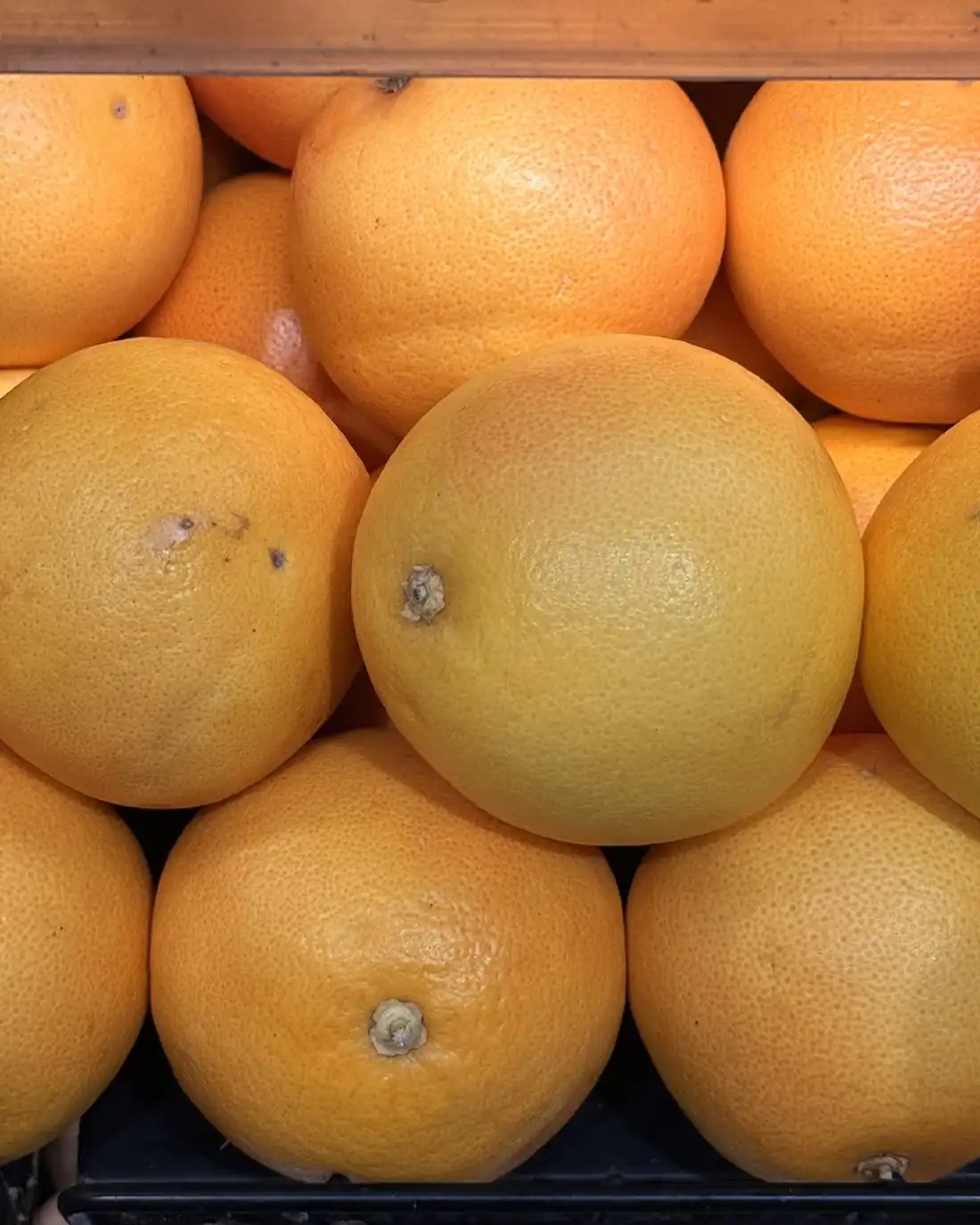 Rows of yellow-orange grapefruits stacked in a market crate