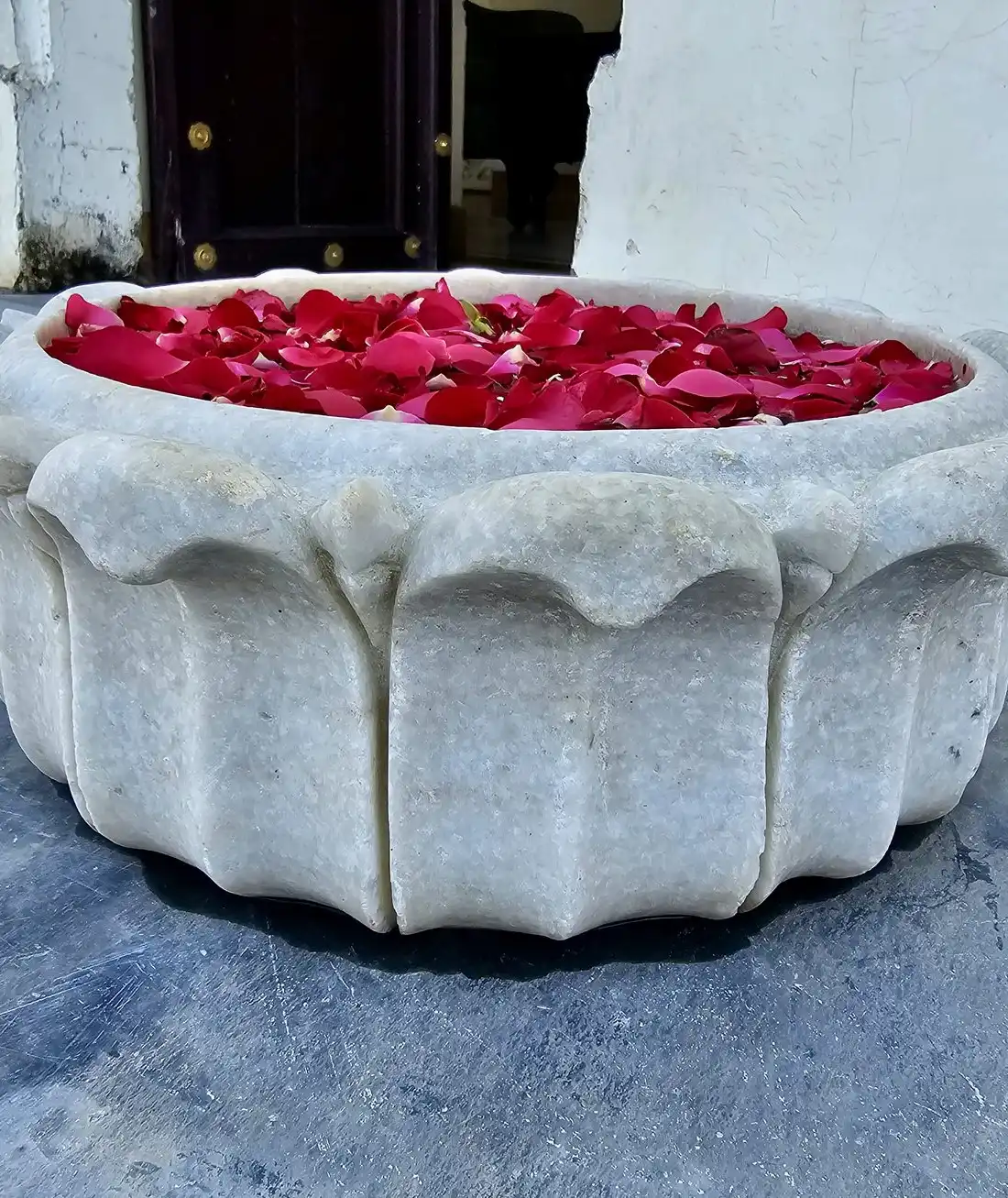 A carved white stone basin filled with red rose petals