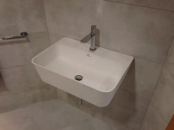 A white wall-mounted basin with a steel tap in a grey tiled bathroom
