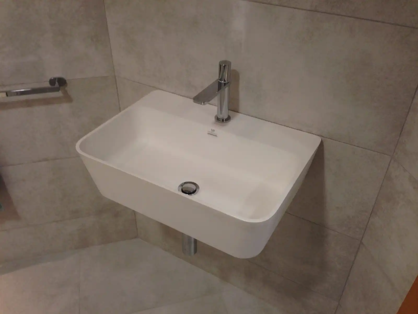 A white wall-mounted basin with a steel tap in a grey tiled bathroom