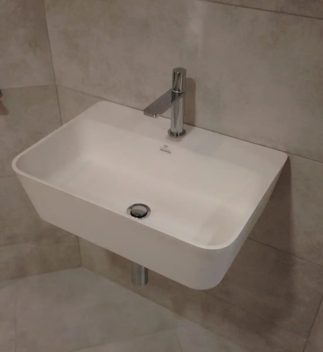 A white wall-mounted basin with a steel tap in a grey tiled bathroom